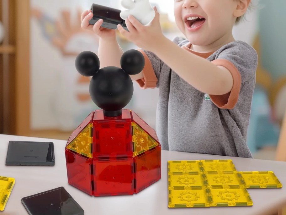 a little boy playing with a magnetic tiles building set that is Mickey Mouse themed and has a Mickey head and arms