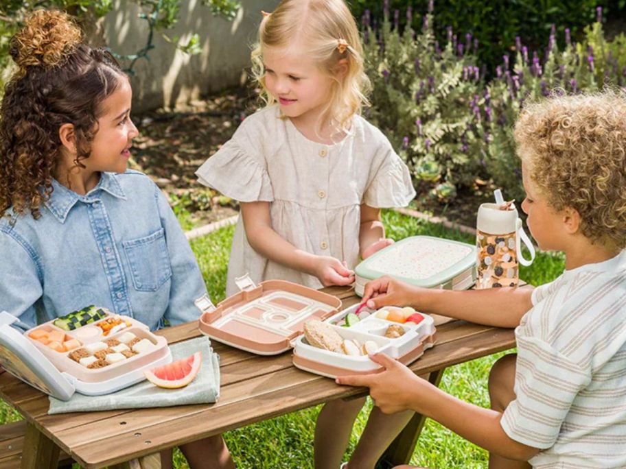 3 kids eating at picnic table with Bentgo lunch boxes