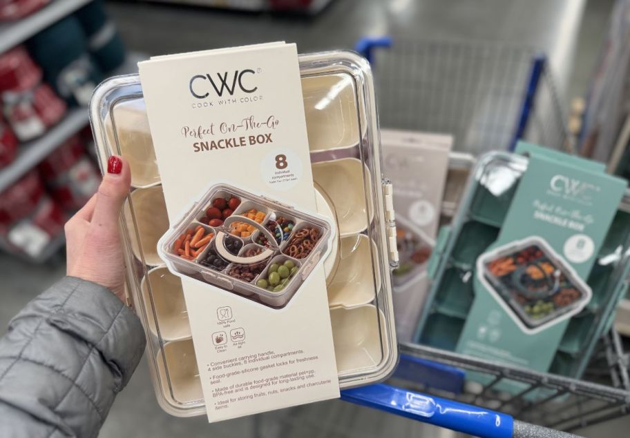 a womans hand holding a cream colored snackle box
