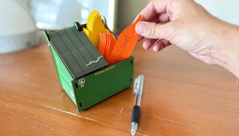 hand holding fire shaped post it note from dumpster on desk