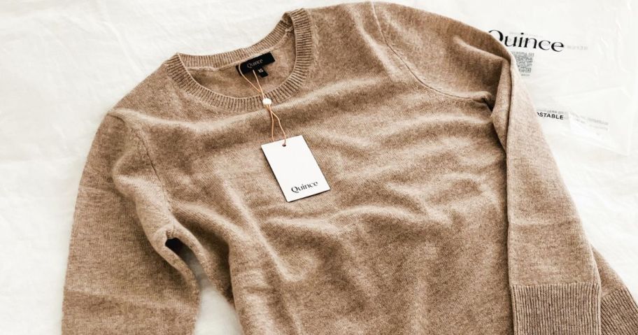 A quince cashmere sweater on a bed