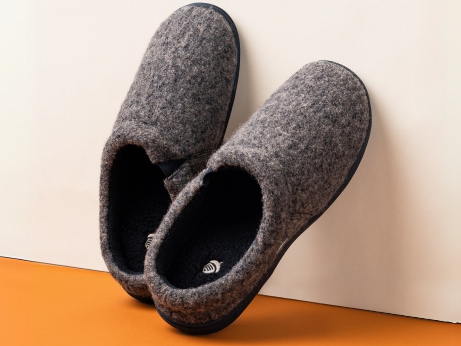 a pair of men's grey slippers leaned up against a wall