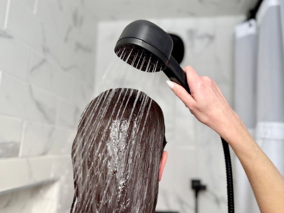 woman rinsing hair with black handheld showerhead 