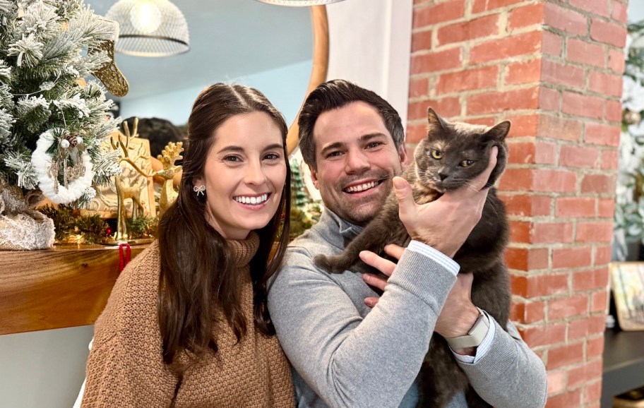 Couple standing with cat in front of brick wall with mirror