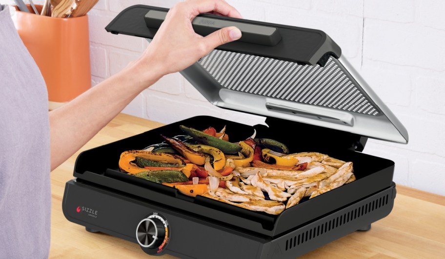 woman opening a ninja sizzle griddle full of onions and peppers