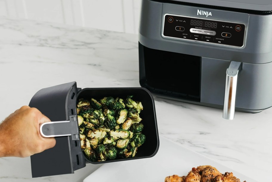 hand on air fryer basket pouring out vegetables