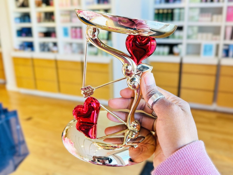 hand holding up a gold and red heats candle holder