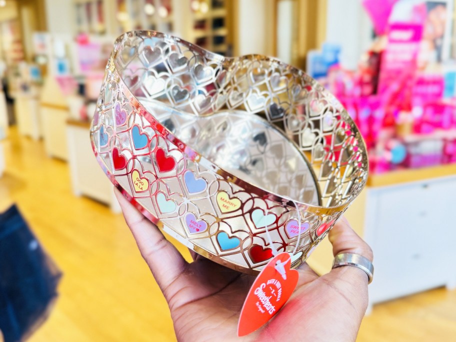 hand holding up a silver heart-shaped tray