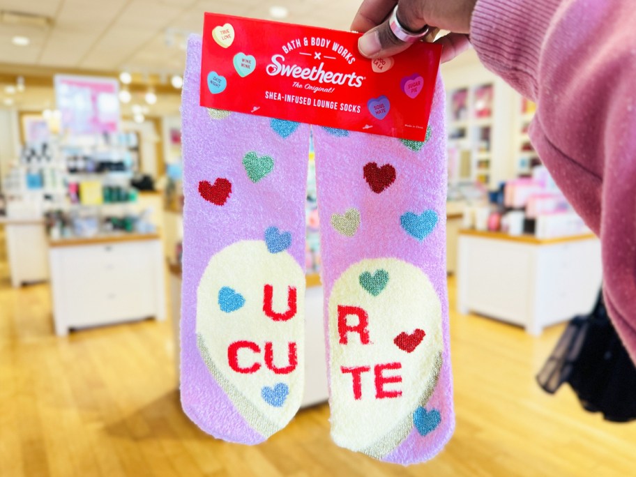 holding up a pair of sweetheart candy print socks that says "u r cute"