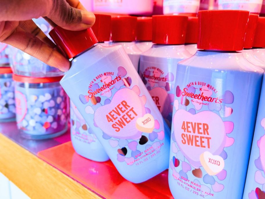 Hand tipping a bottle of Bath & Body Works 4Ever Sweet Body Wash from a row of bottles