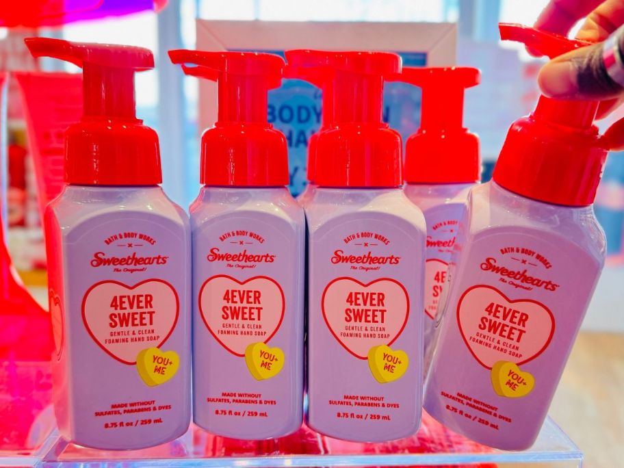Several bottles of Bath & Body Works 4Ever Sweet Hand soap with a human hand tipping one bottle away from the rest