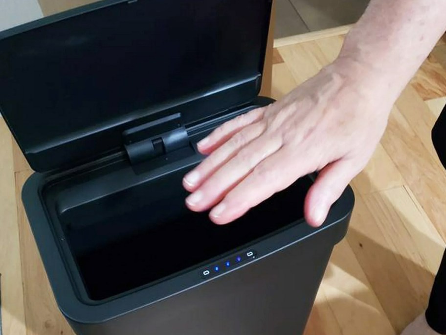 waving hand over black motion sensor trash can