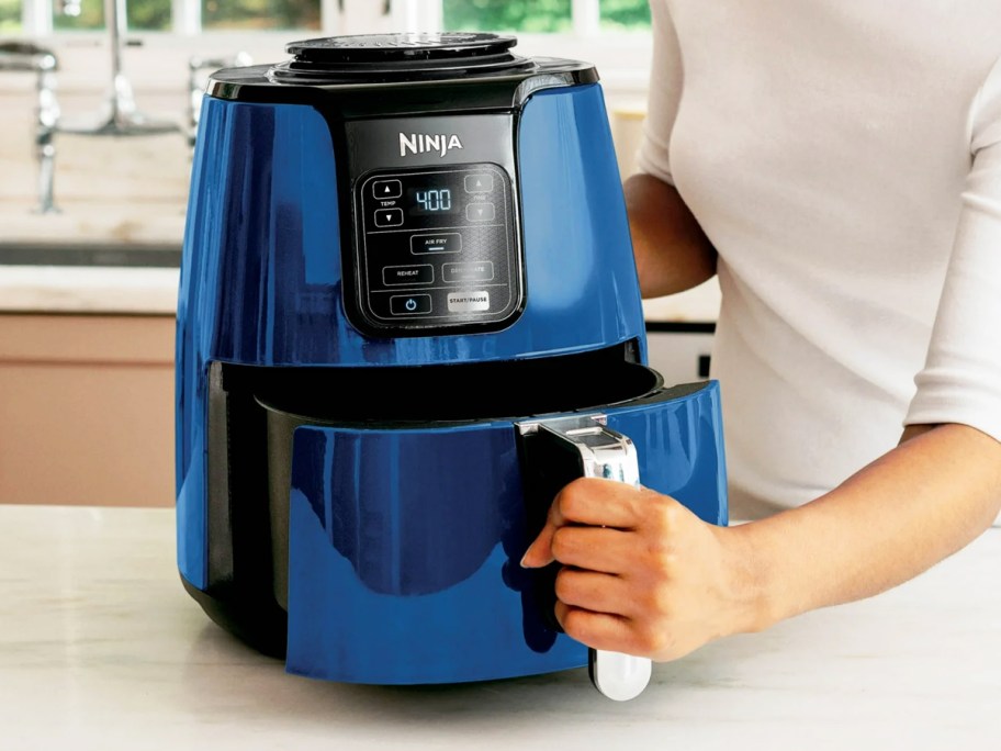 woman opening the basket to a blue and black Ninja air fryer