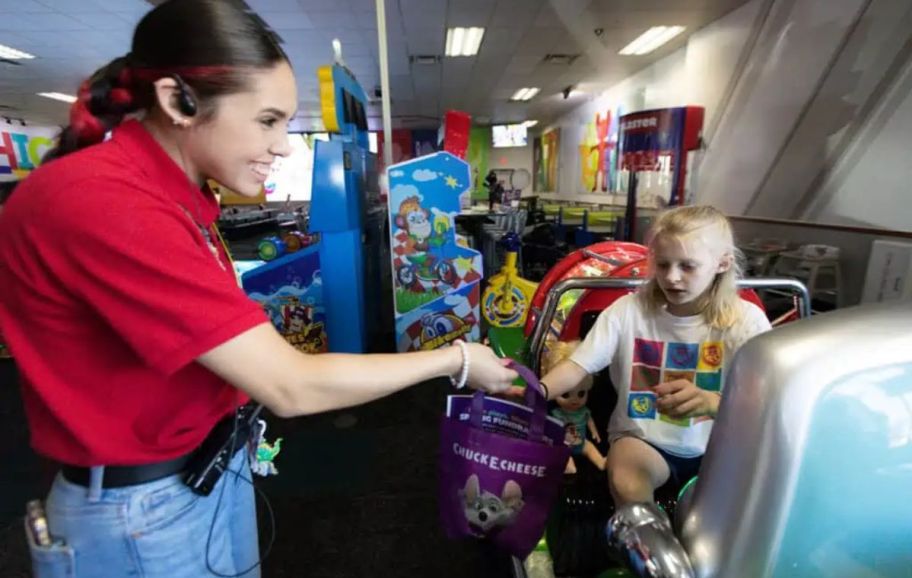 a chuck e cheese employee handing a goody bag to a little girl