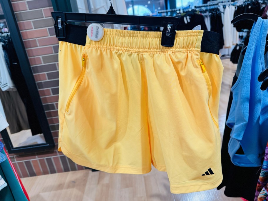 hand holding yellow pair of adidas shorts
