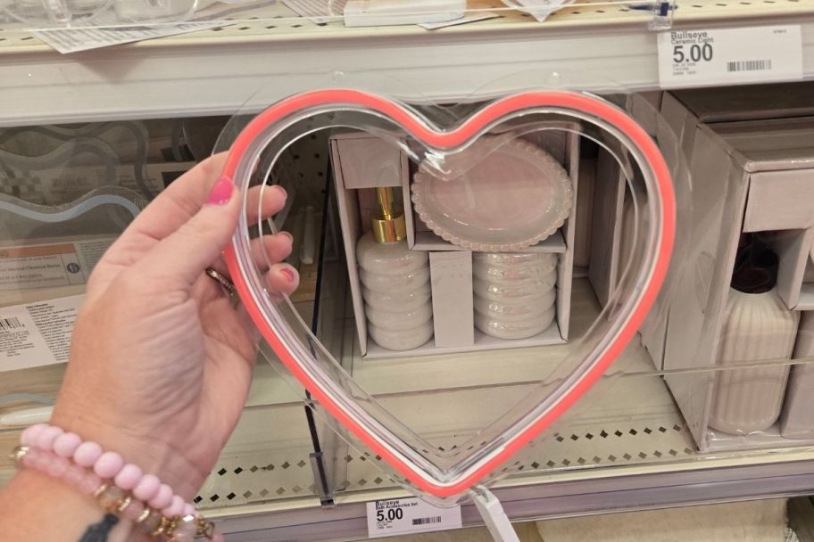 a womans hand holding apink heart shaped faux neon light
