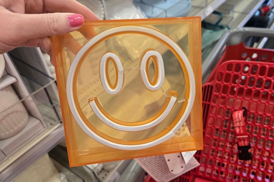 a womans hand holding a square acrylic light with a smiley face design on it