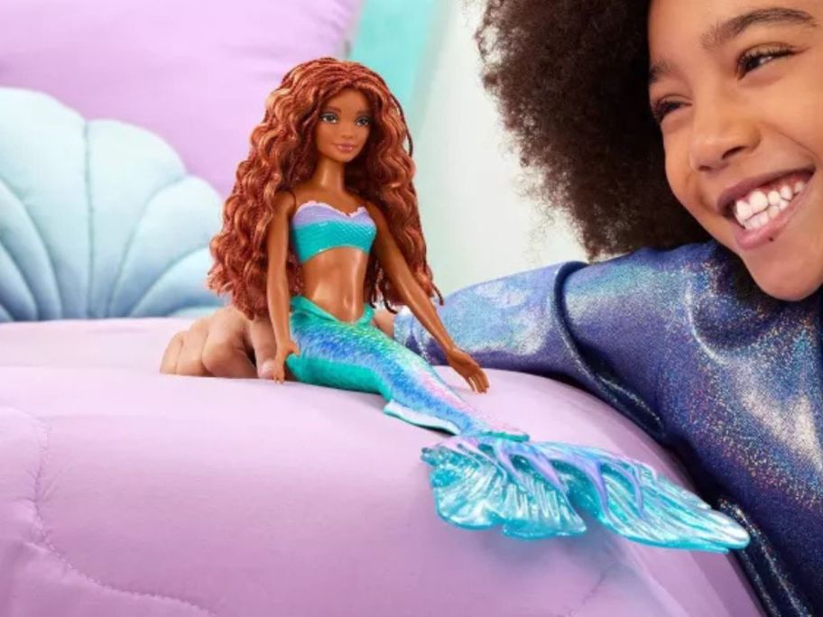 girl looking at Disney The Little Mermaid Ariel Fashion Doll sitting on bed