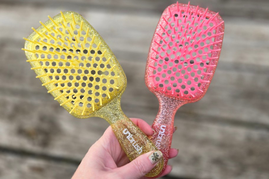 hand holding pink and yellow glitter brushes