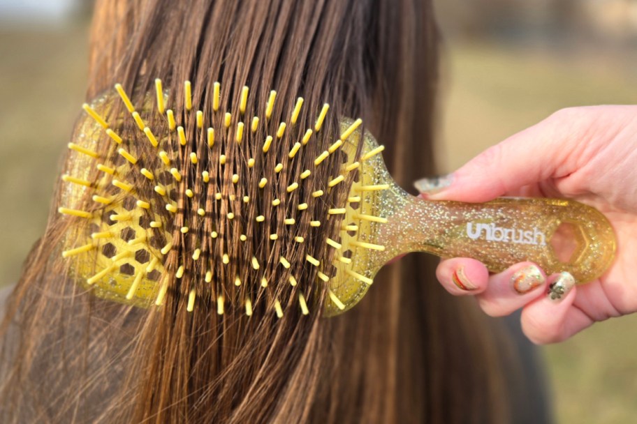hand holding yellow brush brushing girls hair
