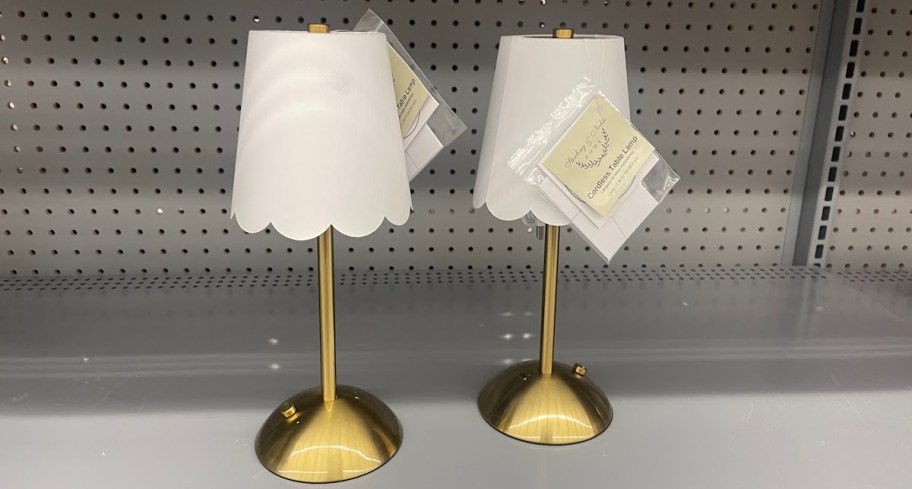 two small scalloped white and brass lamps on store shelf