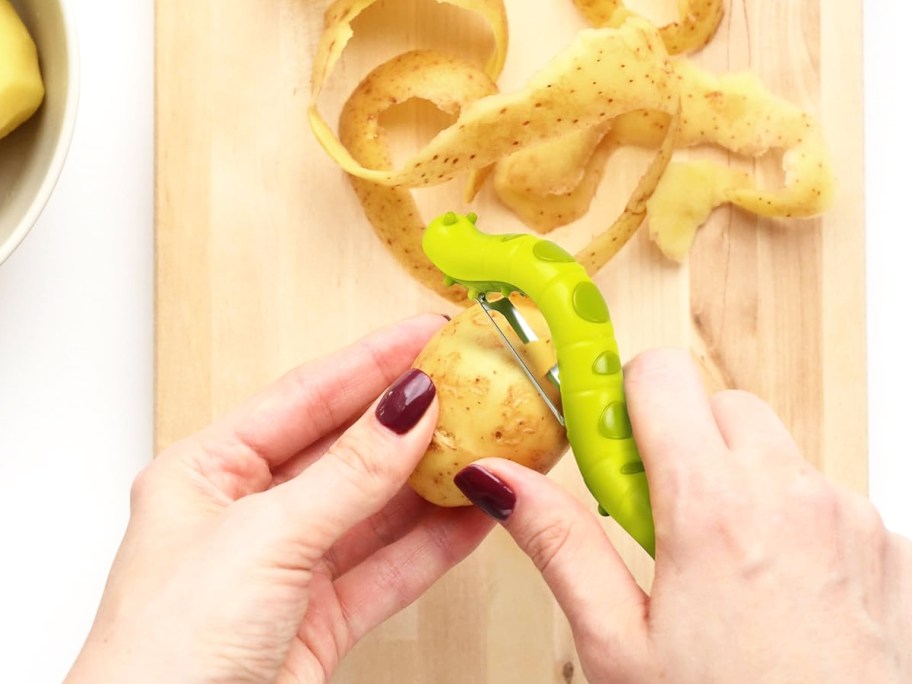 person using a green caterpillar vegetable peeler on a potato
