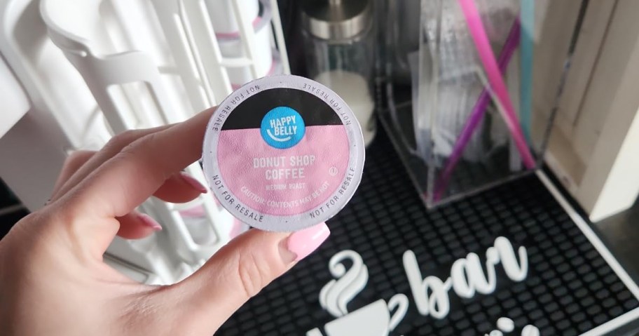 hand holding up a pink donut shop k-cup in front of coffee bar