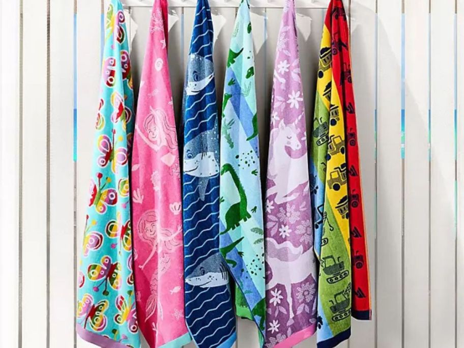 Six Member's Mark Kids Beach Towels hanging on a fence