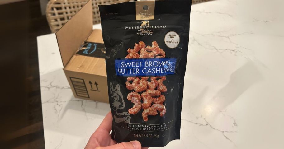 Squirrel Brand Sweet Brown Butter Cashews 3.5oz Bag in hand in front of Amazon box on table