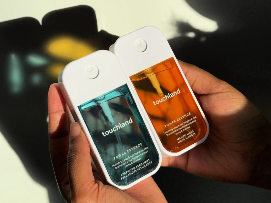 Person holding two bottles of touchland mist in their hand