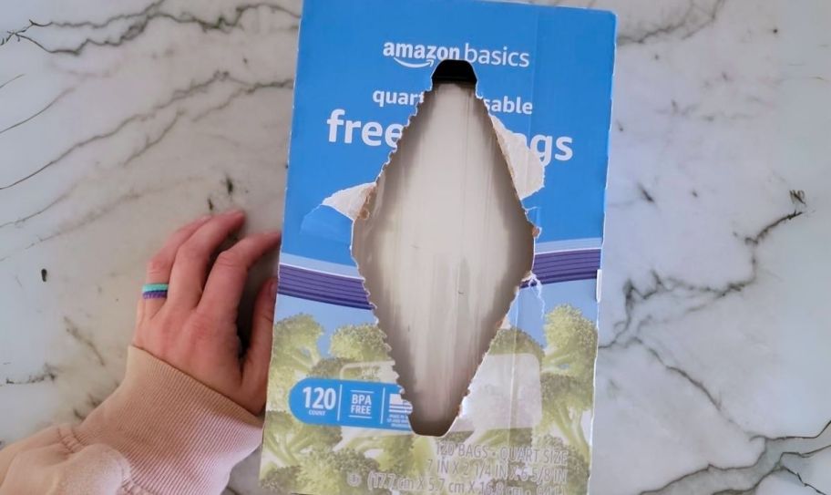 a womans hand next to a box of amazon quart size freezer bags