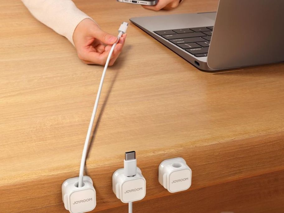 person putting cord into phone from a cord holder attached to desk