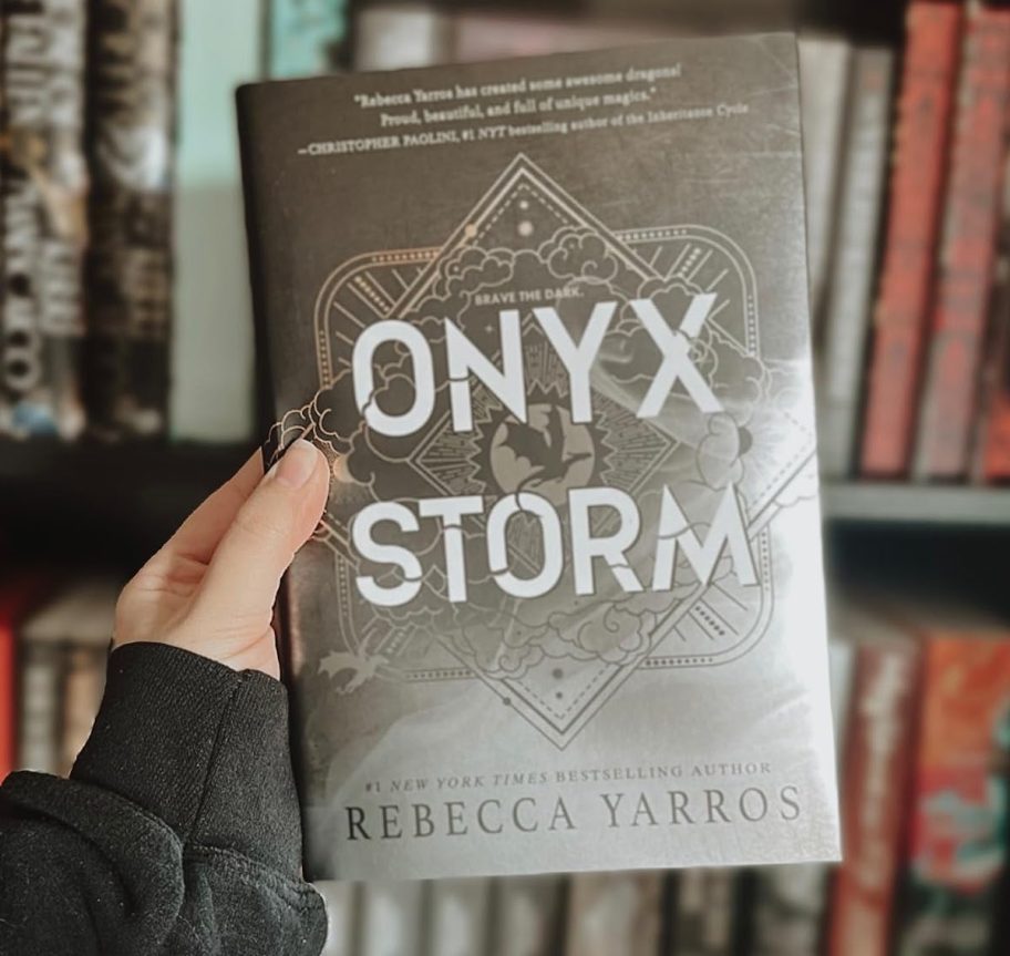 hand holding onyx storm book in front of bookshelf book recommendations 2025
