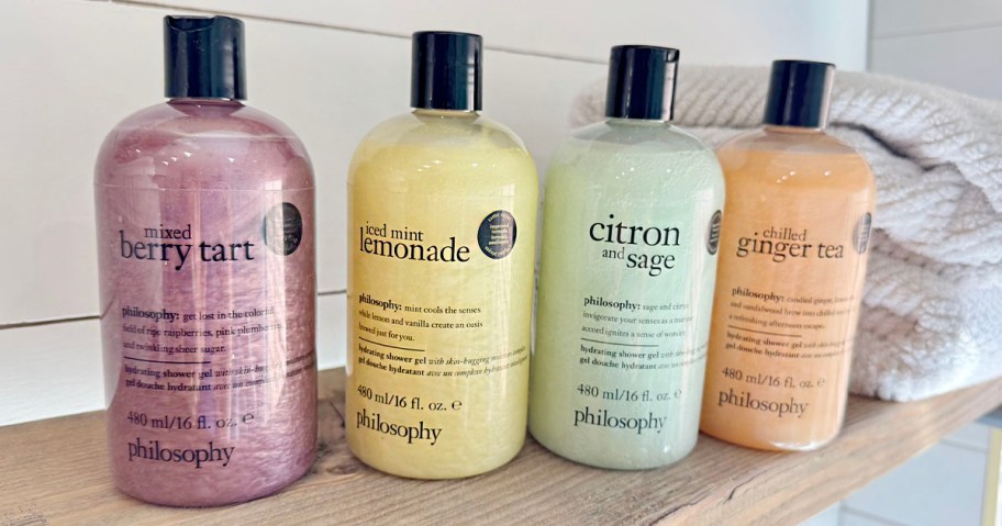 4 philosophy shower gel bottles on table with towel behind them