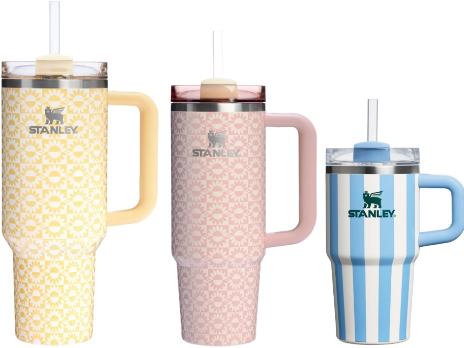 3 Stanley Tumblers in different sizes, one is yellow with a sunburst print, one is pink with a sunburst print, and one is blue and white striped