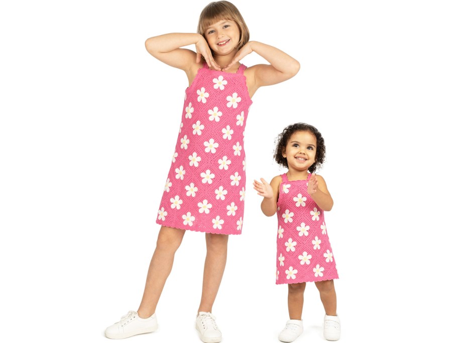 two girls in matching pink crochet dresses with white daisies 