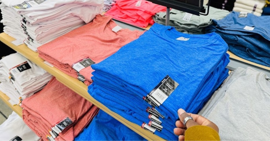 hand reaching for a blue t-shirt on a Walmart display with other colors of t-shirts