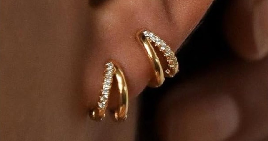 a woman's ear wearing 2 gold and crystal double hoop earrings