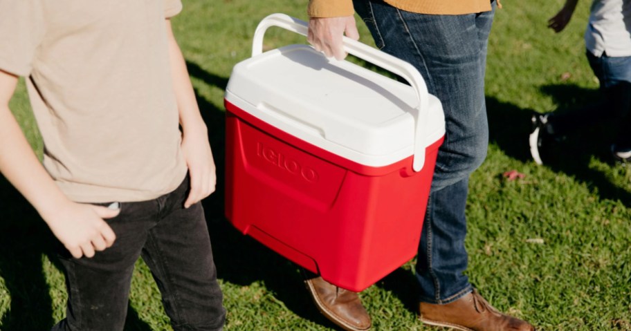 Man carrying red igloo hard cooler while walking in grass
