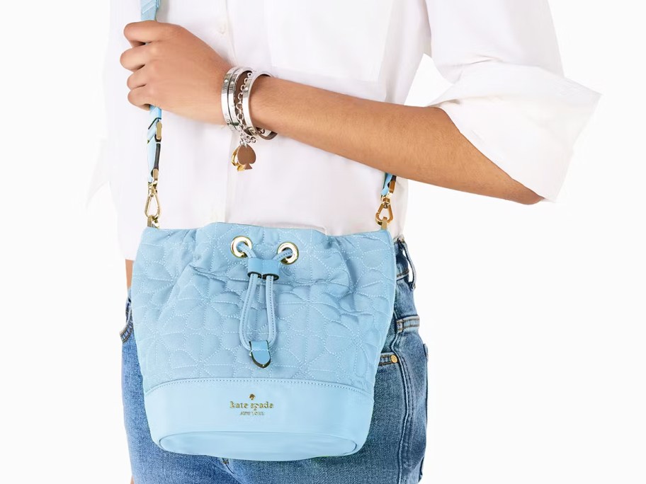 woman in a white top and jeans with a blue flower quilted bucket bag