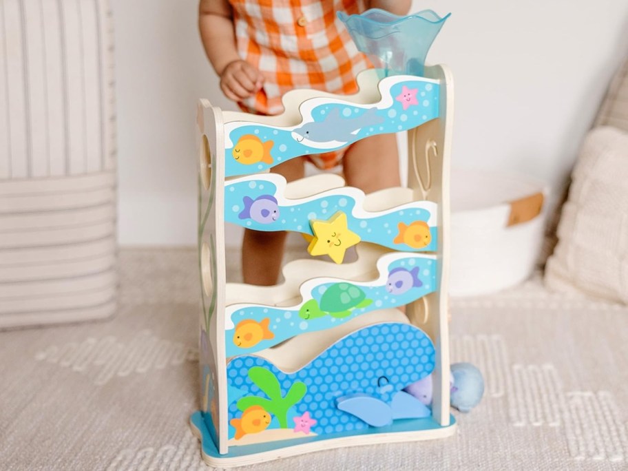 Toddler standing behind Melissa & Doug Ocean Slide Playset.