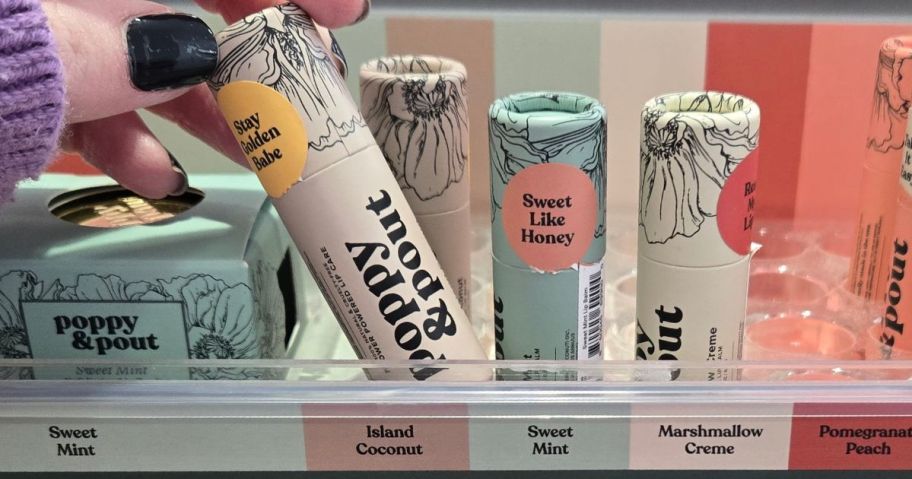hand grabbing a tube of Poppy & Pout Lip Balm from a display