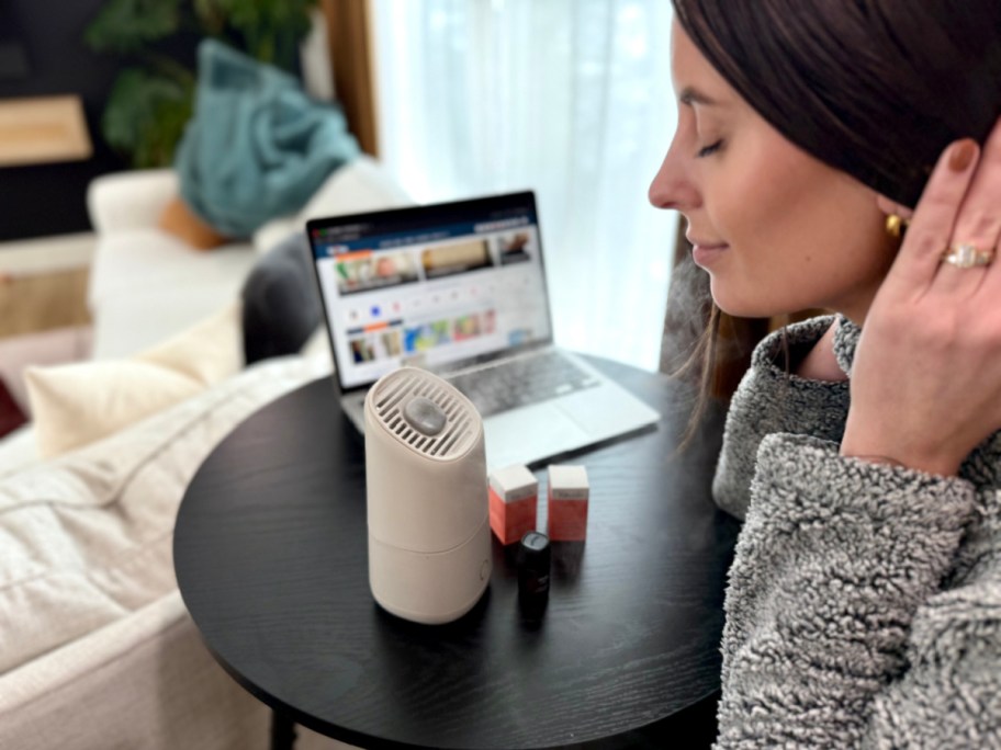 Woman breathing in humidified air from white portable humidifier on desk next to computer