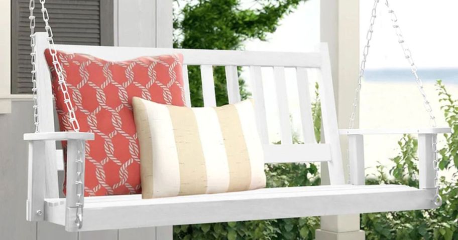 A White porch swing with inviting pillows upon it 