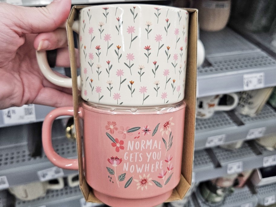 hand holding a set of pink and white floral print coffee mugs with one that says "normal gets you nowhere"
