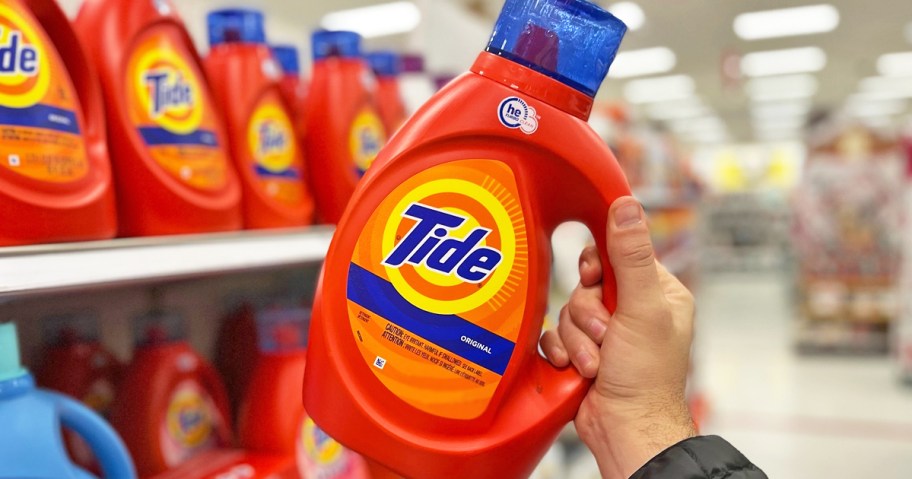 hand grabbing an orange bottle of Tide Original Laundry Detergent from store shelf