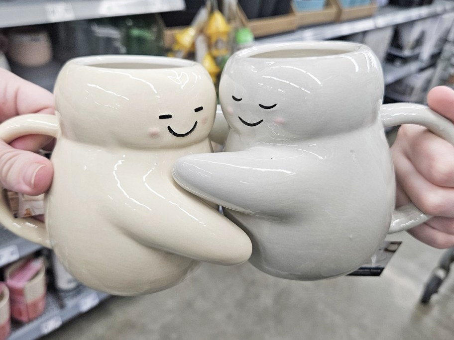 hands holding up coffee mugs that are hugging