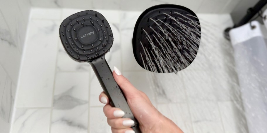 hand holding black showerhead with water coming out of fixed showerhead