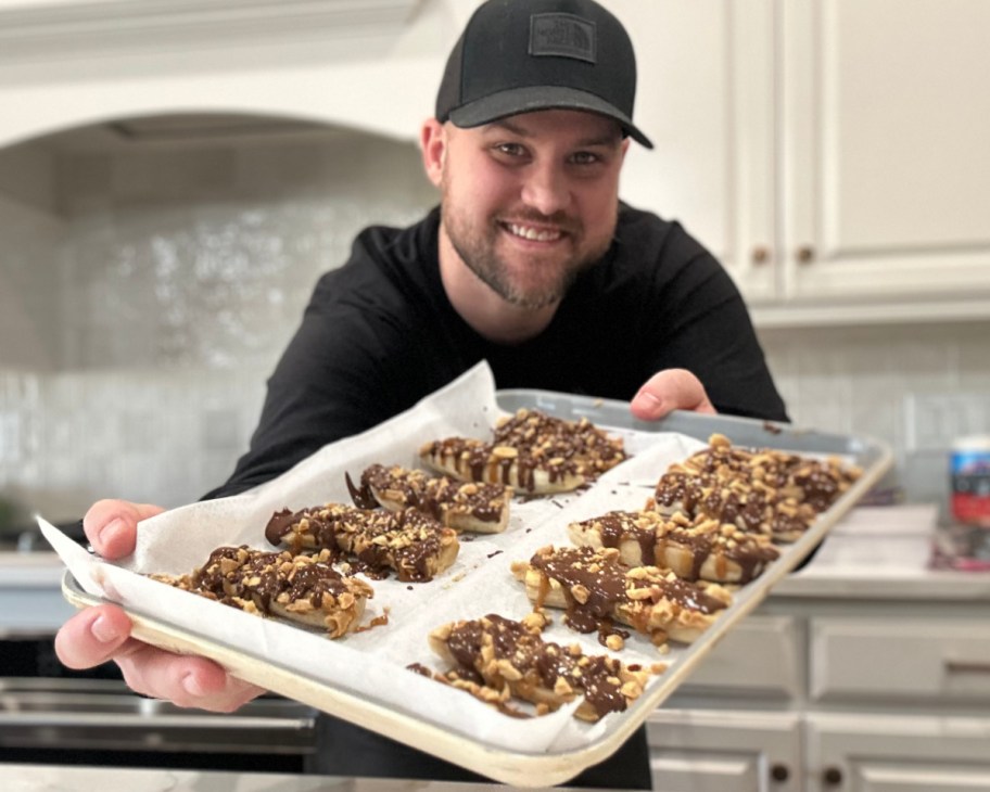 man holding cookie sheet with frozen bananas covered in chocolate
