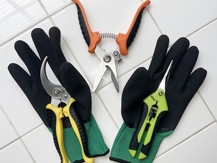 pair of green and black garden gloves with three garden shears laying with them